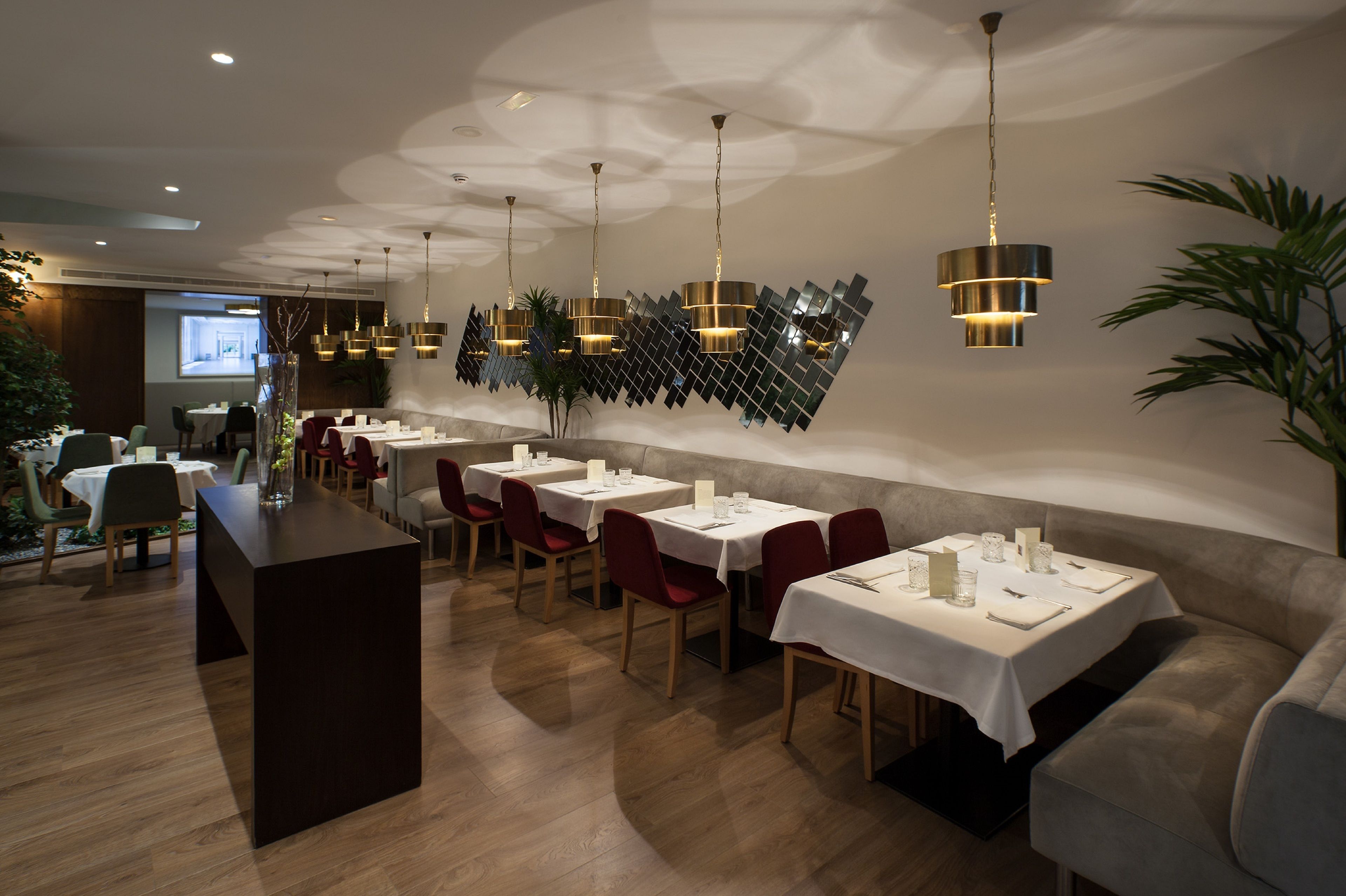 A modern restaurant interior with wooden flooring, white tablecloths, red chairs, and pendant lighting.