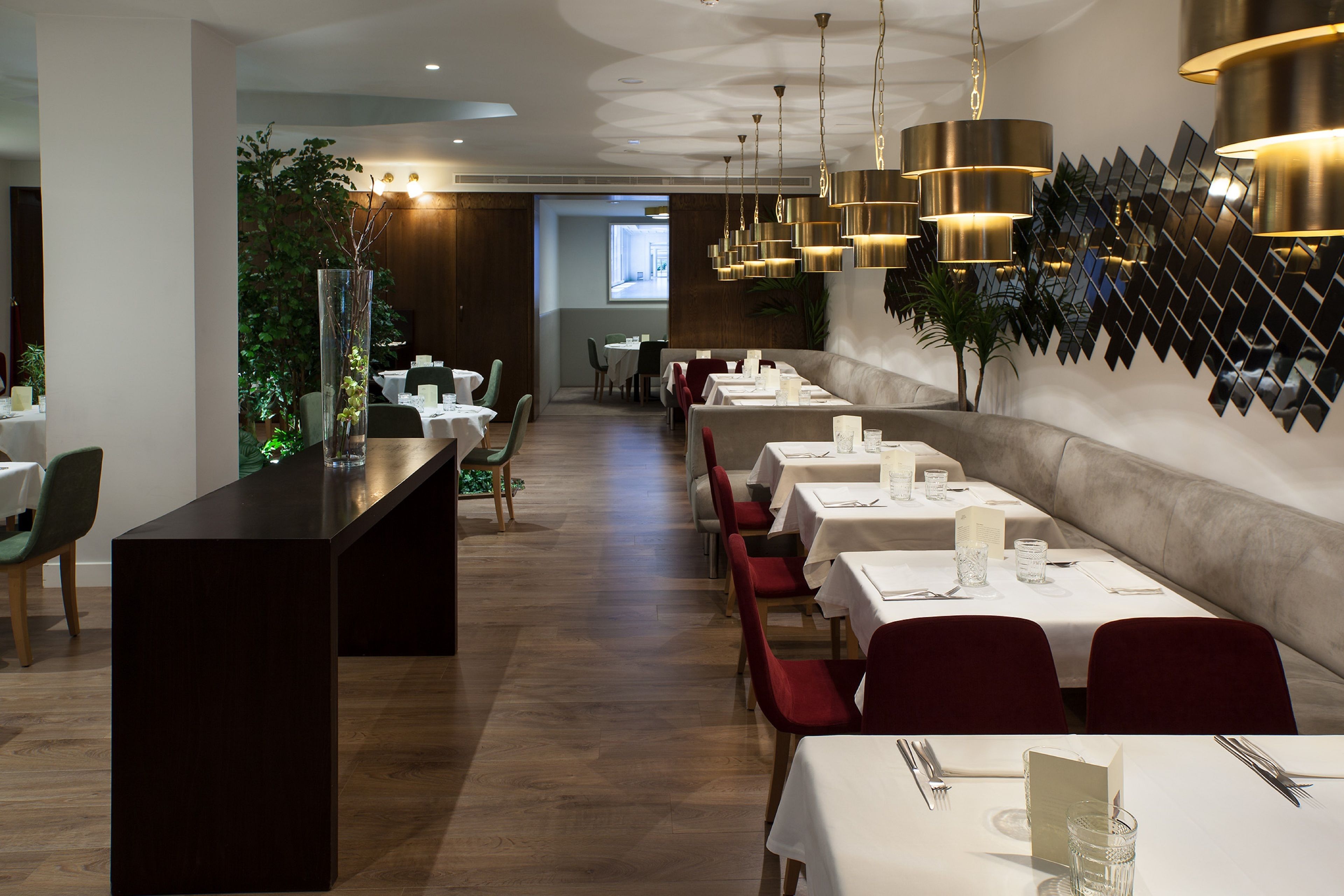 A restaurant with a long counter, multiple tables, and red chairs.