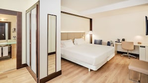 A hotel room with a large bed, a desk, a chair, a mirror, and a bathroom visible through a glass door. - NH Madrid Lagasca (Madrid)