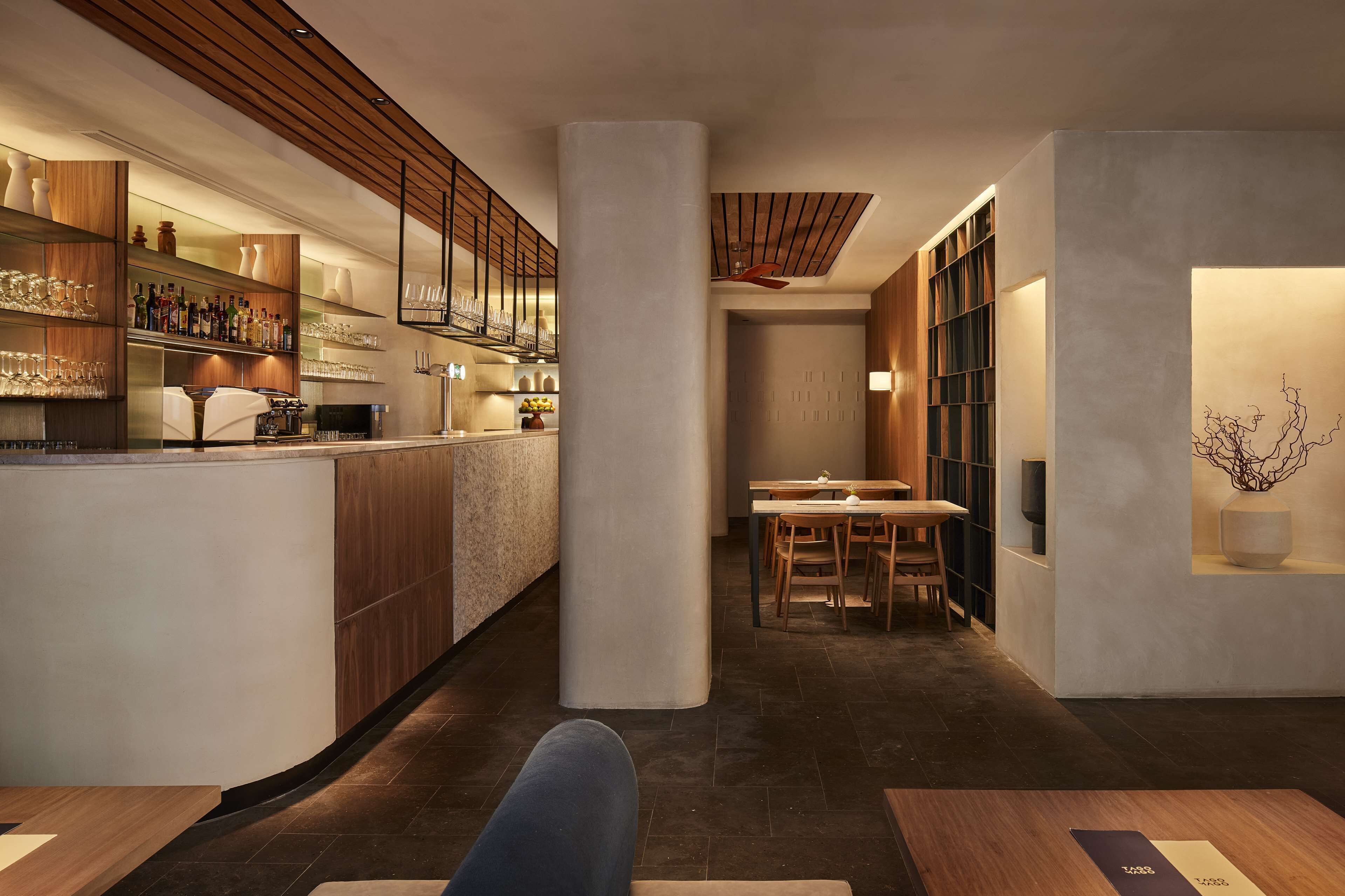 Un área de bar moderna con estantes de madera, una barra y un espacio de asiento con mesas y sillas.