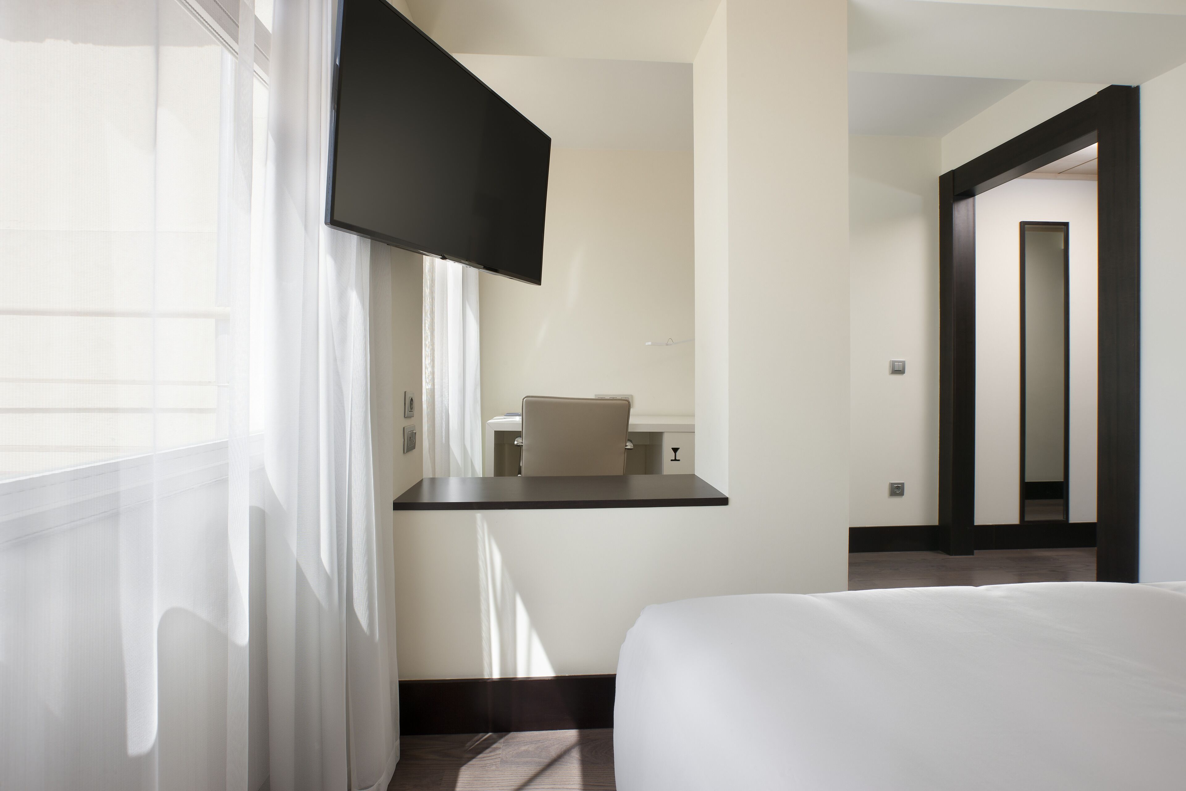 A hotel room with a bed, a TV mounted on the wall, a small table, and a chair.