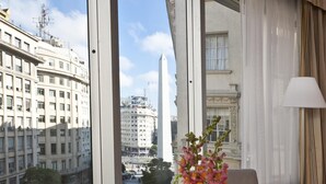 Une chambre d’hôtel avec une grande fenêtre, une table ronde, un vase de fleurs et une lampe.