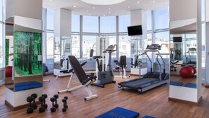 Une salle de sport moderne dotée de divers équipements d’exercice, de grandes fenêtres et offrant une vue sur la ville.