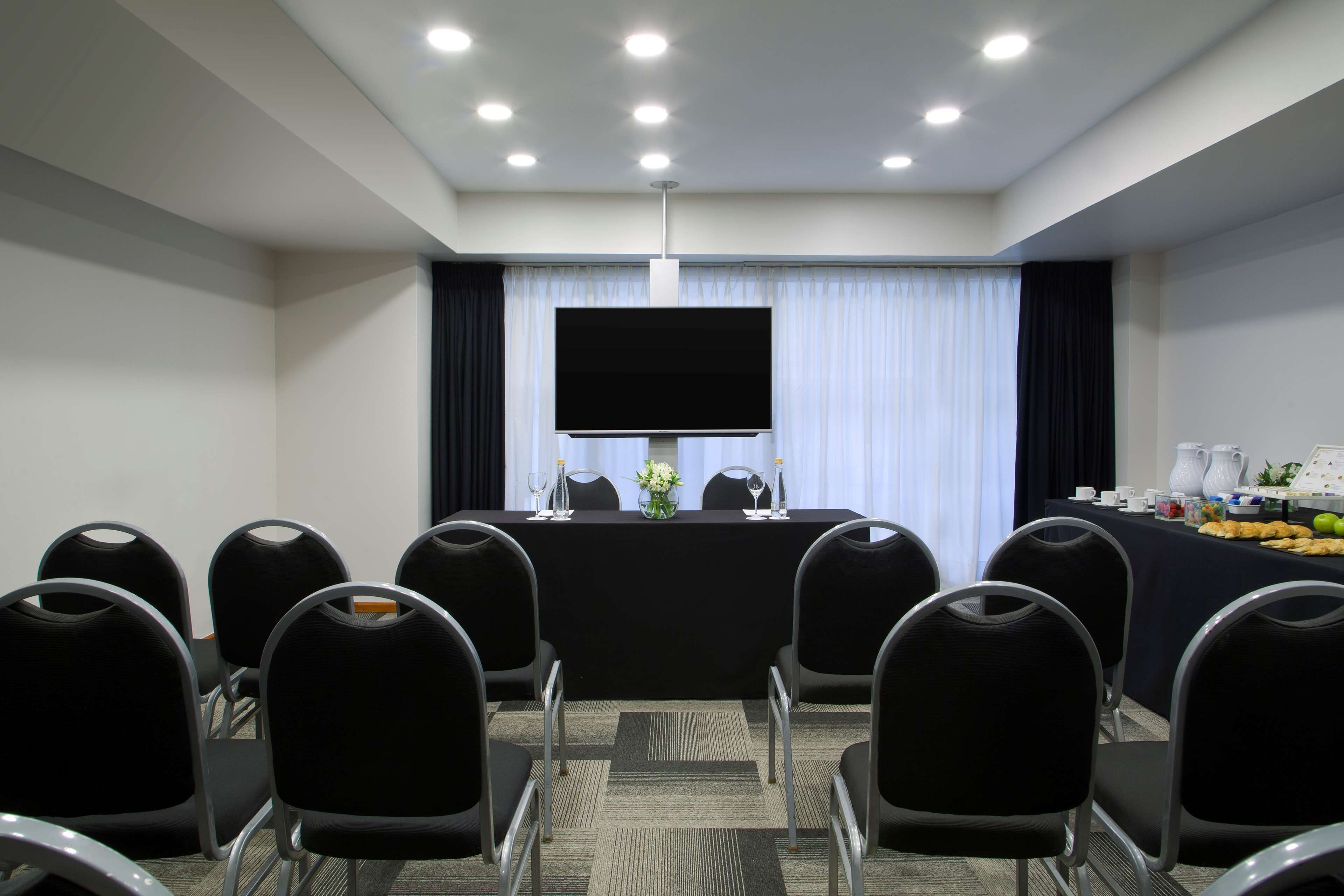 Un salón de conferencias con una gran televisión de pantalla plana, una mesa con un centro de mesa floral y una mesa de buffet con comida y bebidas.