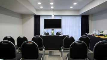 Un salón de conferencias con una gran televisión de pantalla plana, una mesa con un centro de mesa floral y una mesa de buffet con comida y bebidas.