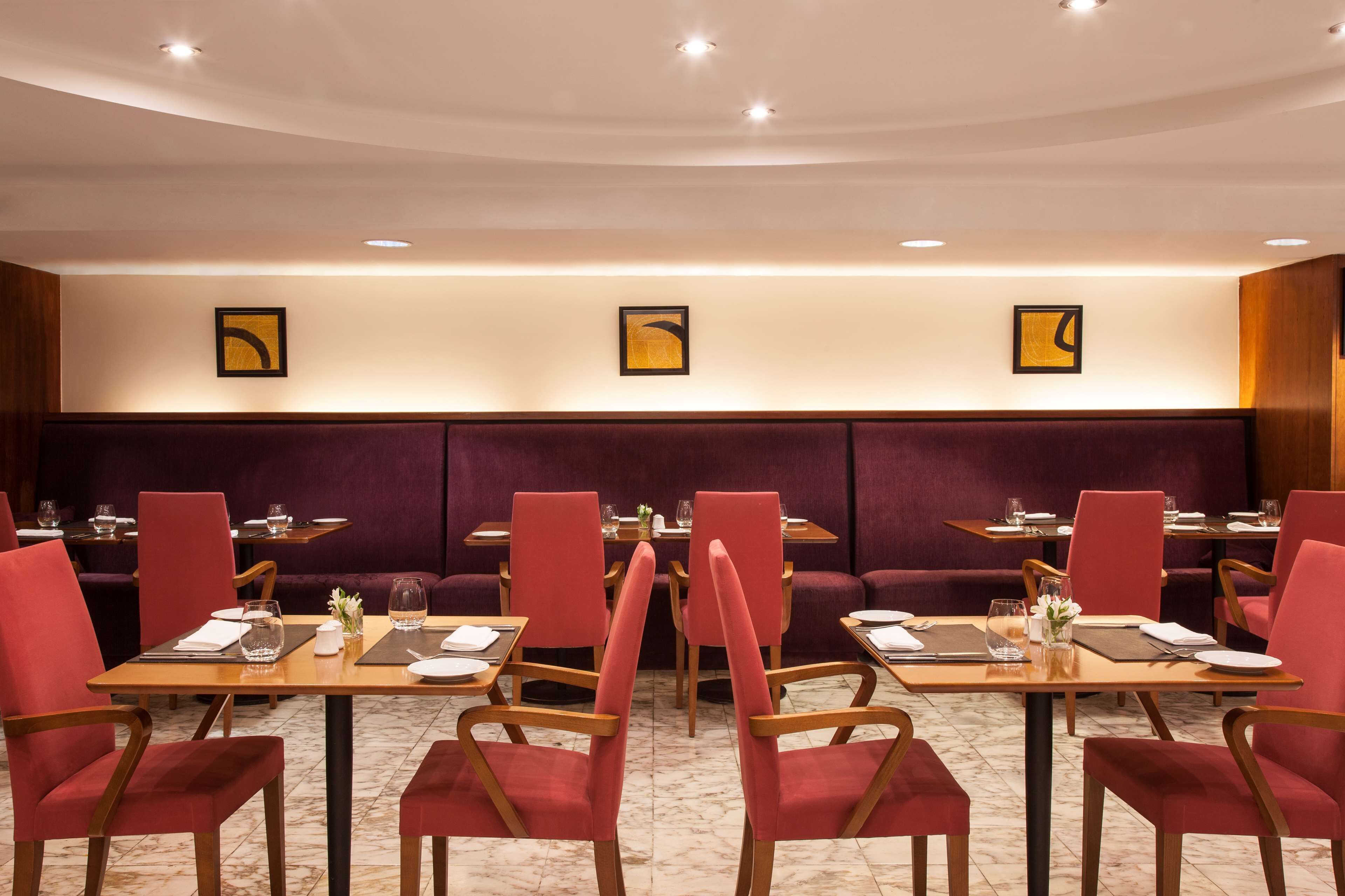 Un restaurante con sillas tapizadas en rojo, mesas de madera y suelo de mármol.