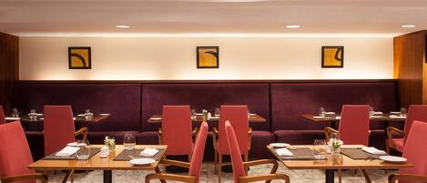 Un restaurante con sillas tapizadas en rojo, mesas de madera y suelo de mármol.