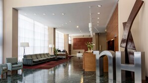 Un hall d’entrée spacieux avec un comptoir d’accueil moderne, un coin salon avec des canapés et une grande sculpture en forme de H.