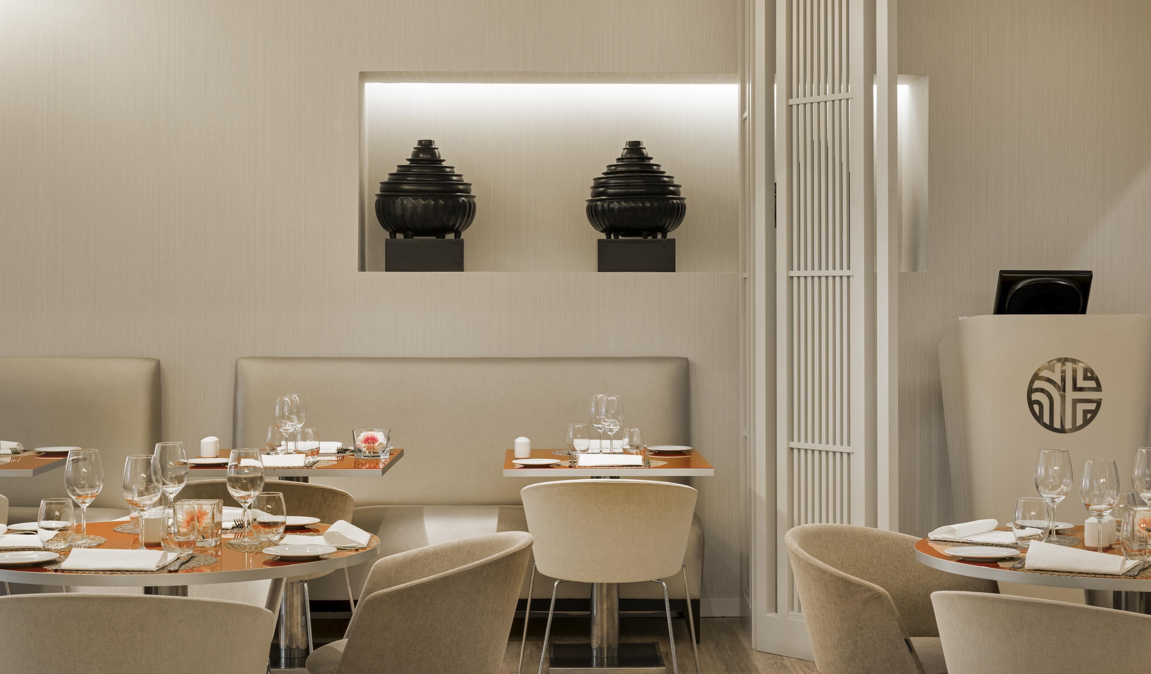 Um restaurante com decoração moderna, apresentando uma área de jantar central com mesas e cadeiras redondas, e uma área separada com assentos tipo camarote.