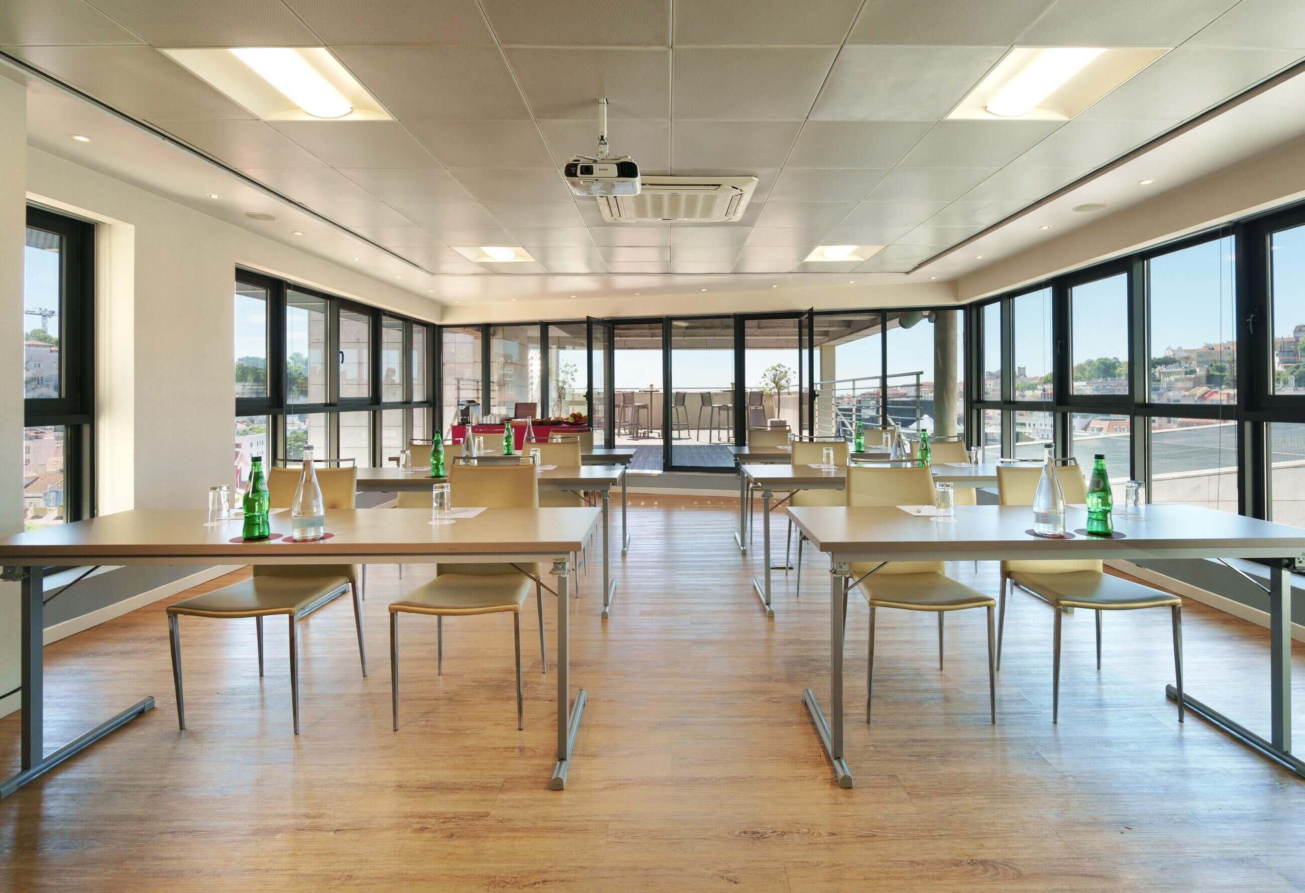 Una amplia sala de conferencias con ventanas grandes, un proyector y varias mesas y sillas.