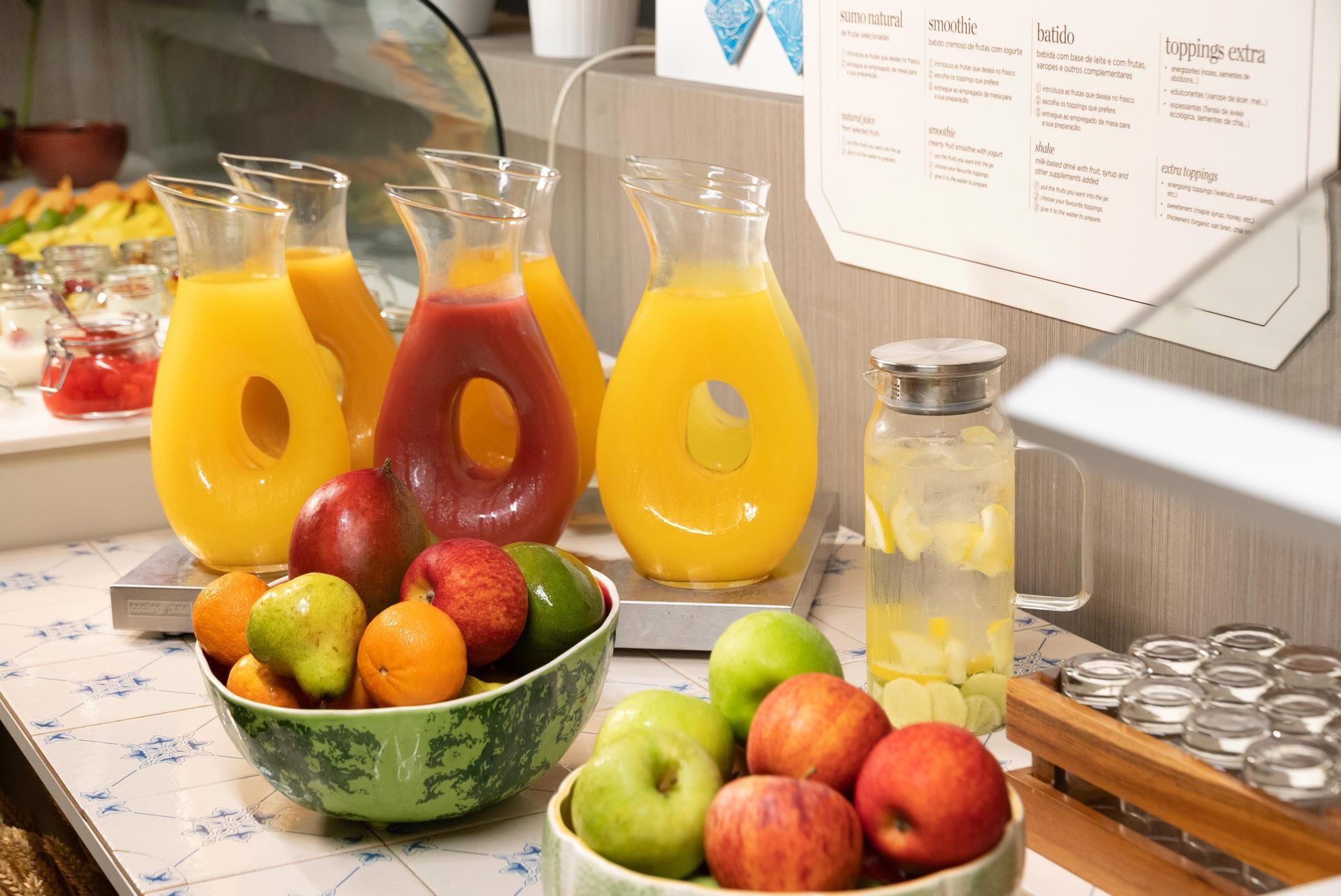 Un buffet de petit-déjeuner proposant un assortiment de jus de fruits, de fruits frais et un tableau affichant le menu.