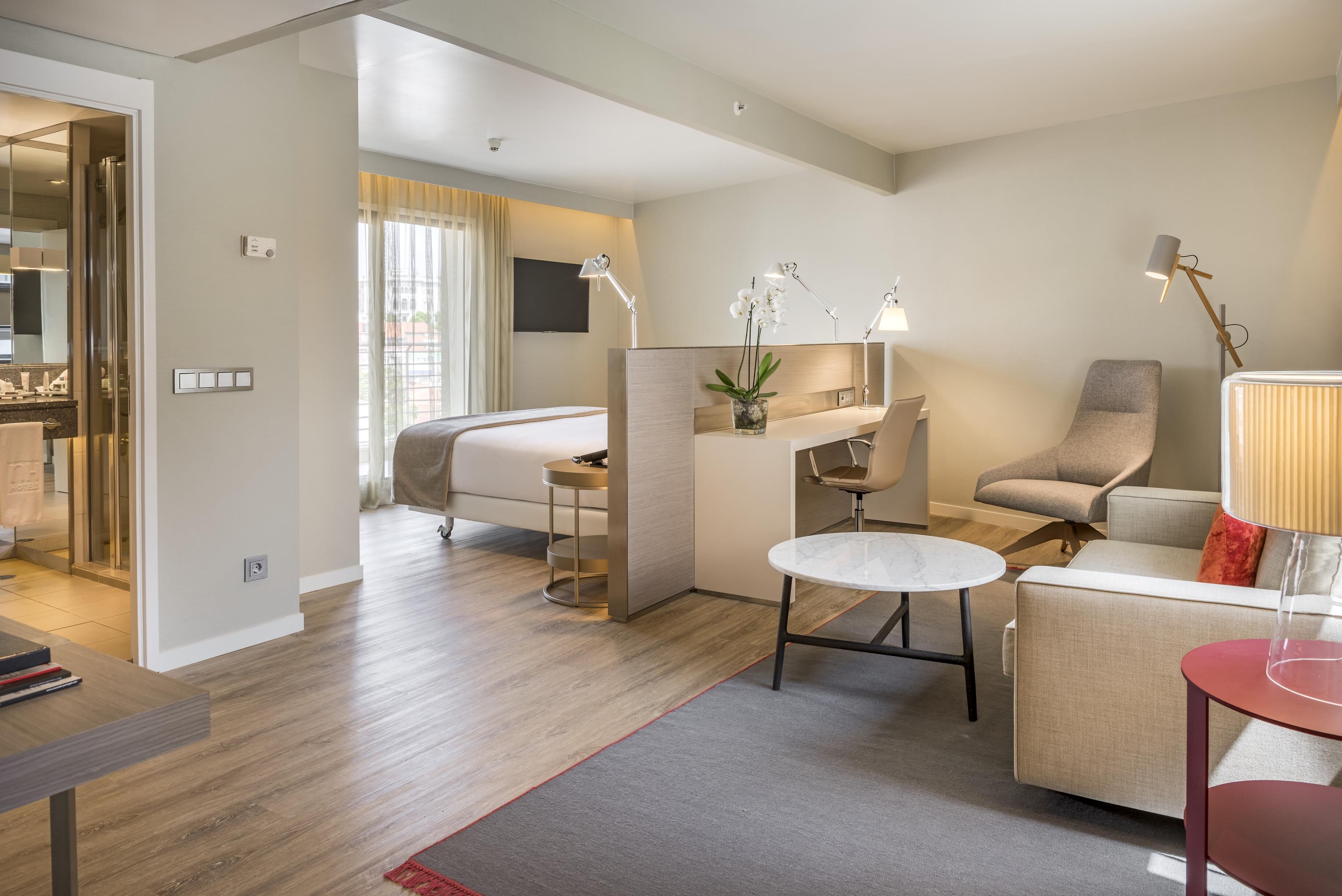 A modern hotel room with a bed, desk, chair, and a small table.