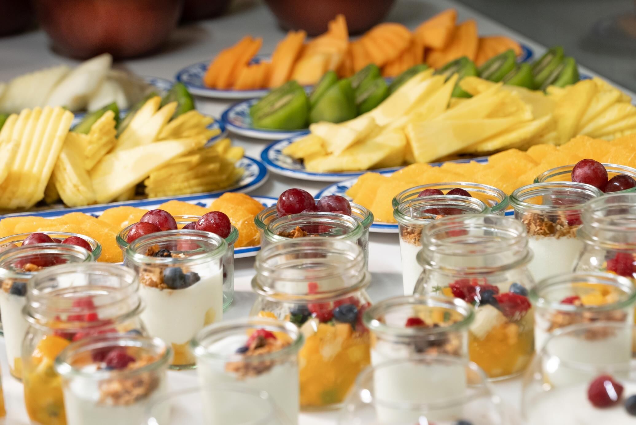 Un bufé con diversas frutas, verduras y pequeños recipientes de yogur con frutos rojos.