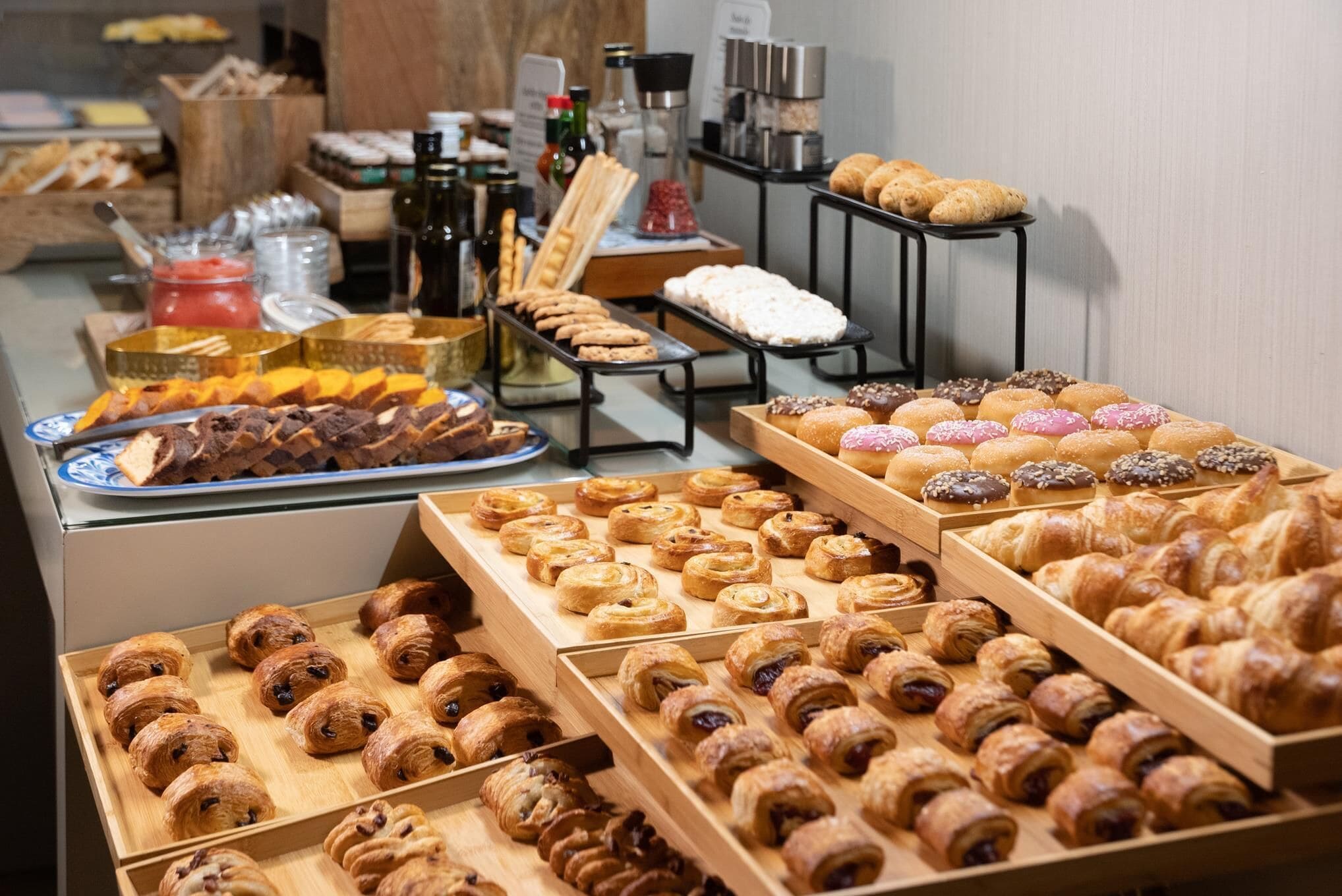 Un'ampia varietà di dolci e prodotti da forno esposti su vassoi e tavoli di legno, con salse e bevande sullo sfondo.