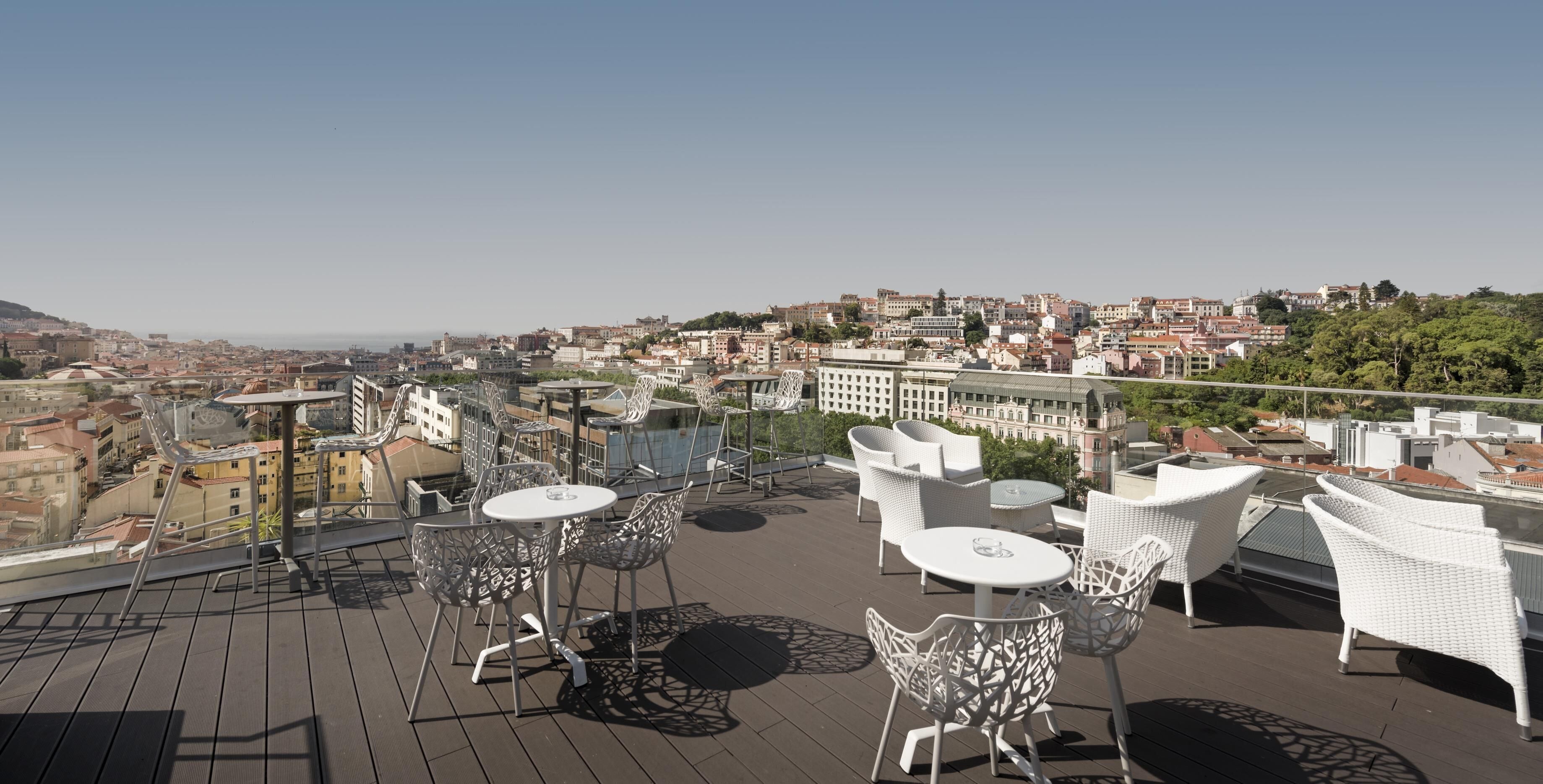 Terraza en la azotea con mobiliario de mimbre blanco y una vista despejada del paisaje urbano.