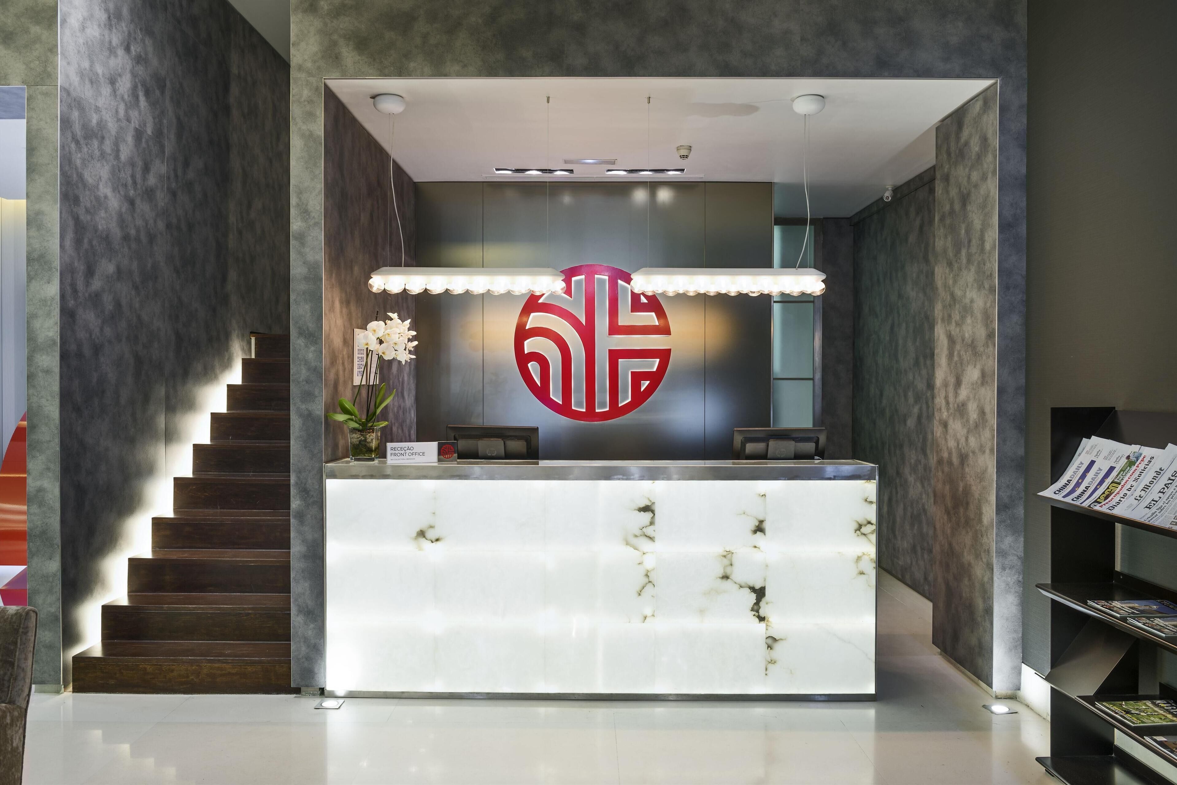 A modern reception desk with a marble top, a large circular logo, and a staircase to the left.
