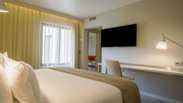 A hotel room with a bed, bedside lamps, a TV, a desk, and a chair.