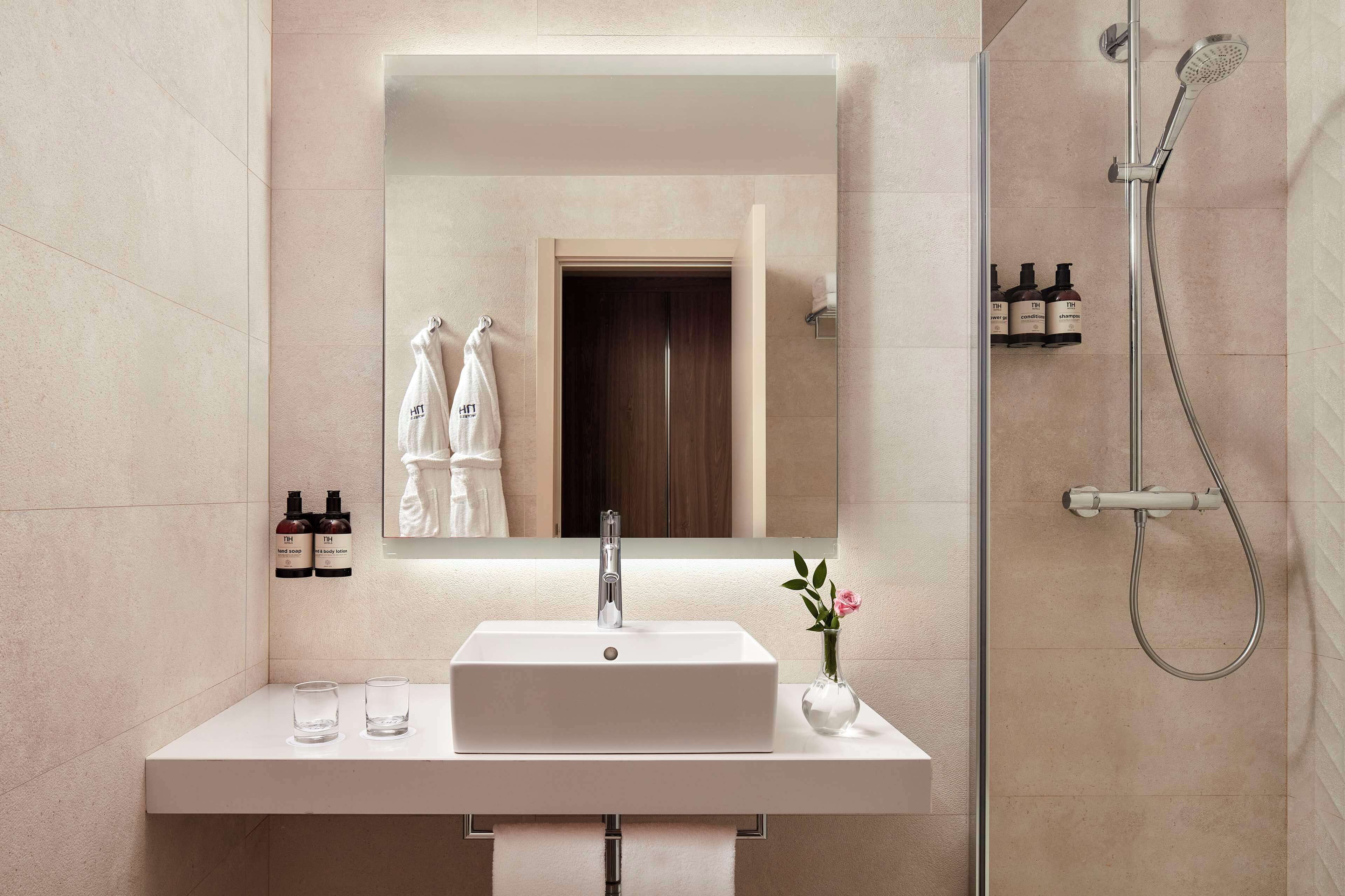 Un baño moderno con un lavamanos rectangular, un espejo, un cabezal de ducha manual y un pequeño florero con una flor.