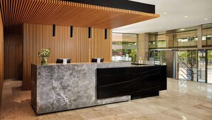 A reception area with a marble counter, wooden slats, and a view of the outdoors. - NH Luz Huelva (Huelva)