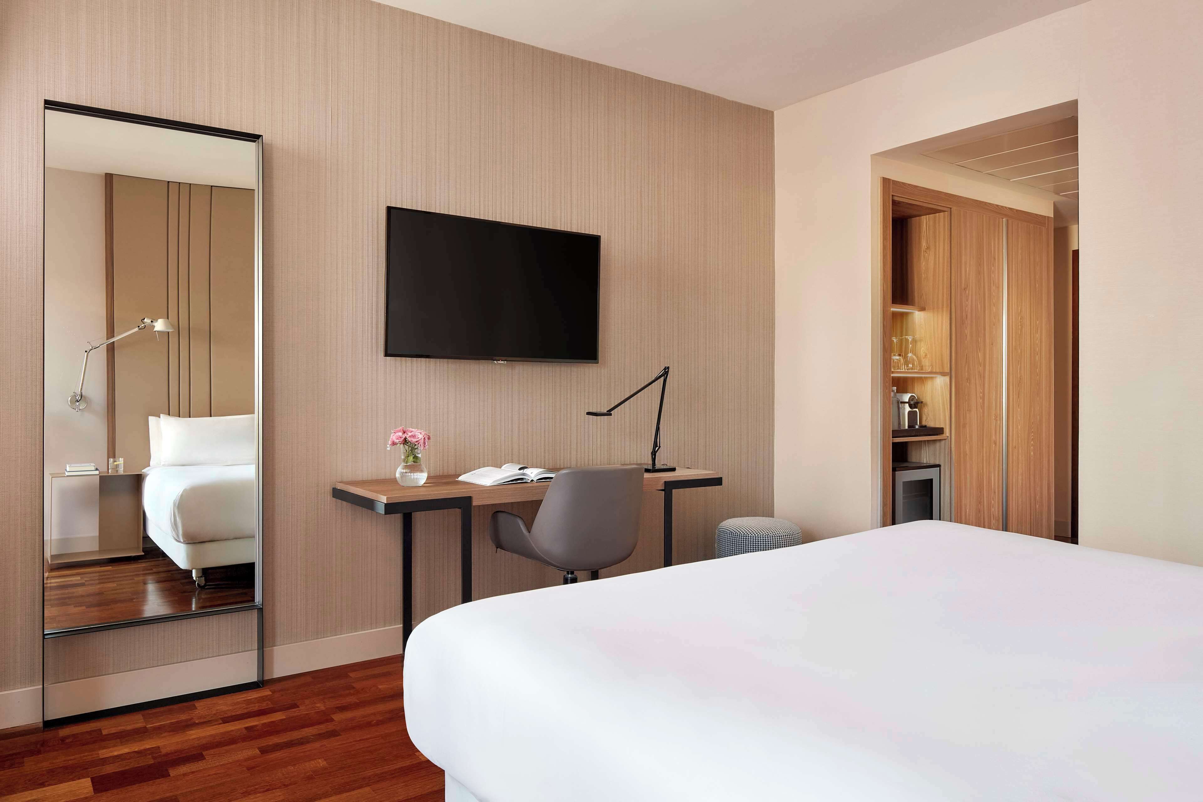Une chambre d’hôtel avec un lit, un bureau et une chaise, une télévision et un miroir.