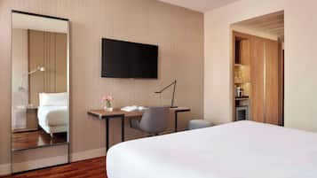 A hotel room with a bed, a desk with a chair, a TV, and a mirror.