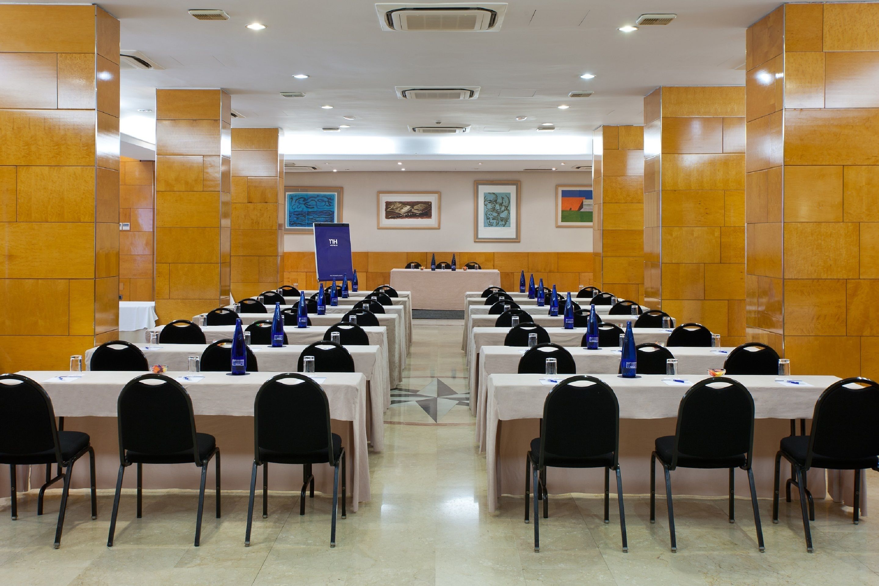 A conference room with multiple tables and chairs, arranged in rows, with a podium at the front.