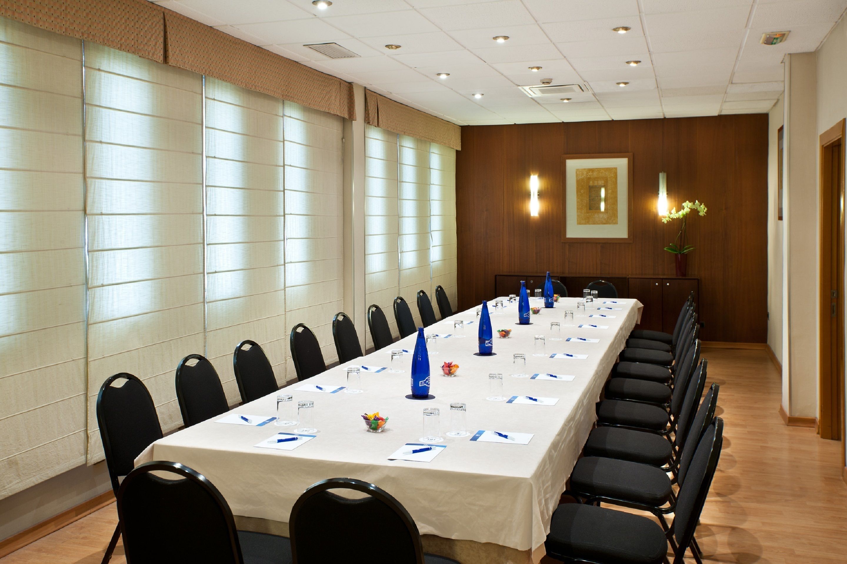 Un salón de conferencias con una larga mesa, sillas negras y un mantel blanco.