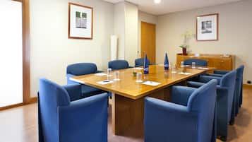Una sala de conferencias con una mesa de madera, sillas azules, cuadros en las paredes y un aparador con un teléfono.