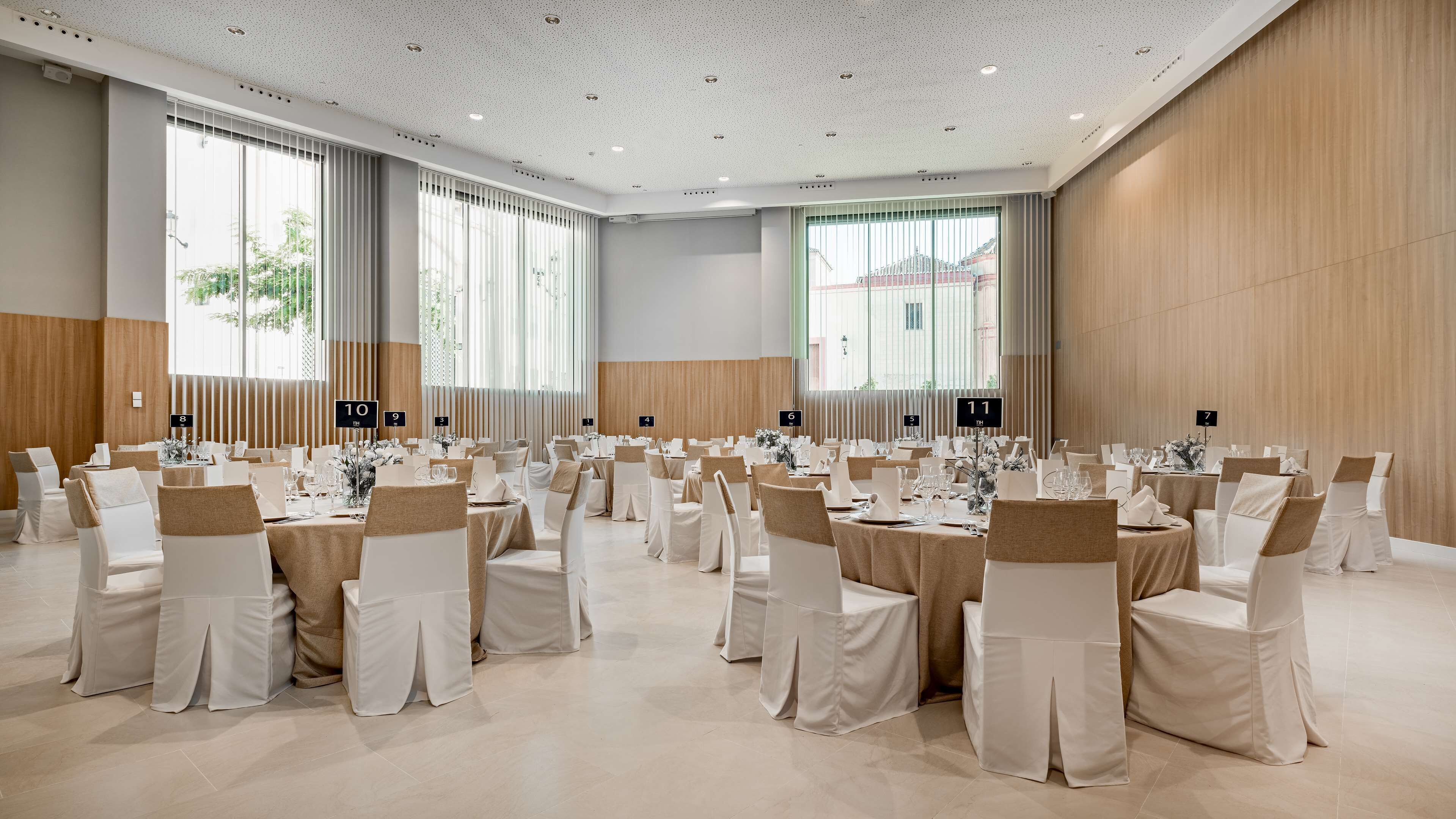 Ein großer Festsaal mit mehreren runden Tischen, jeder Tisch mit weißer Tischdecke und Stühlen gedeckt, und mit Hinweisschildern, die die Tischordnung angeben.