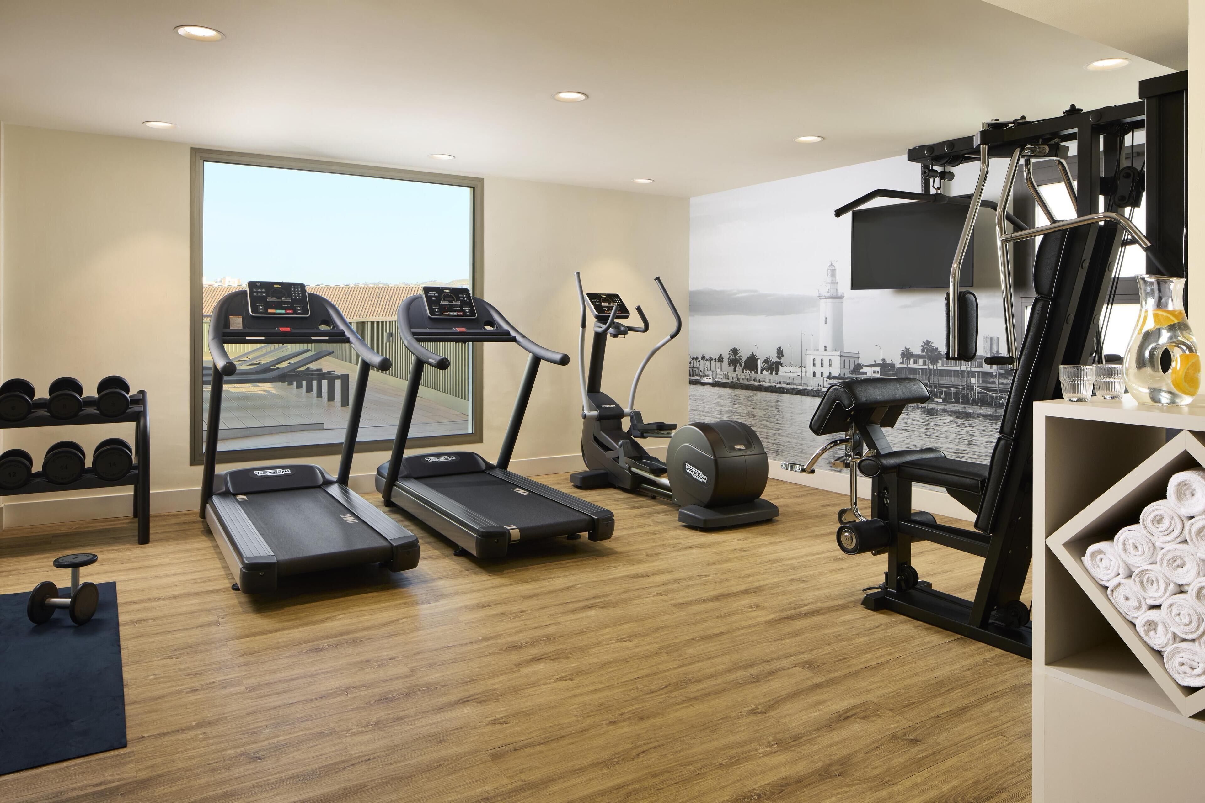 Un gimnasio moderno con cintas de correr, elípticas y pesas libres.
