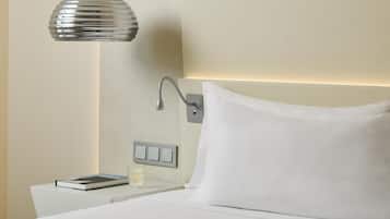 A neatly made bed with white linens, a bedside table with a book and a glass, and a wall-mounted light fixture.