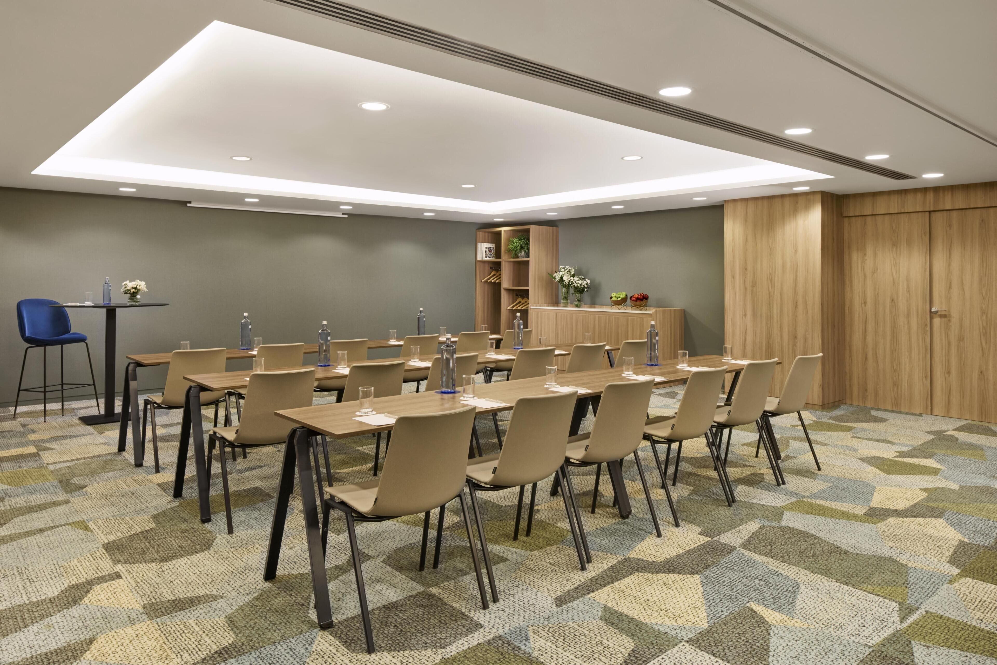 Un salón de conferencias con una larga mesa, sillas, una pequeña zona de bar y un armario de madera con plantas.