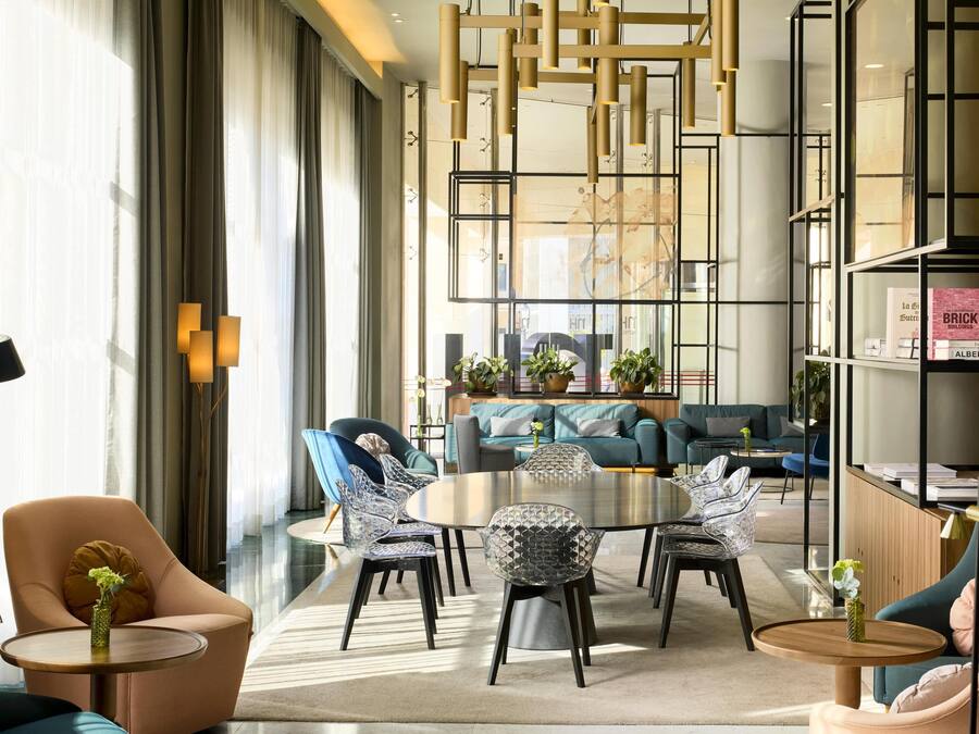 Un moderno vestíbulo de hotel con una mesa de comedor redonda, sofás y una estantería.