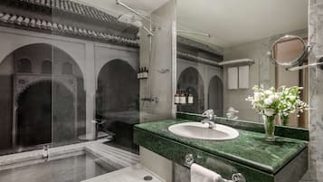 Un baño moderno con un lavamanos de mármol verde, un espejo grande y una zona de ducha.