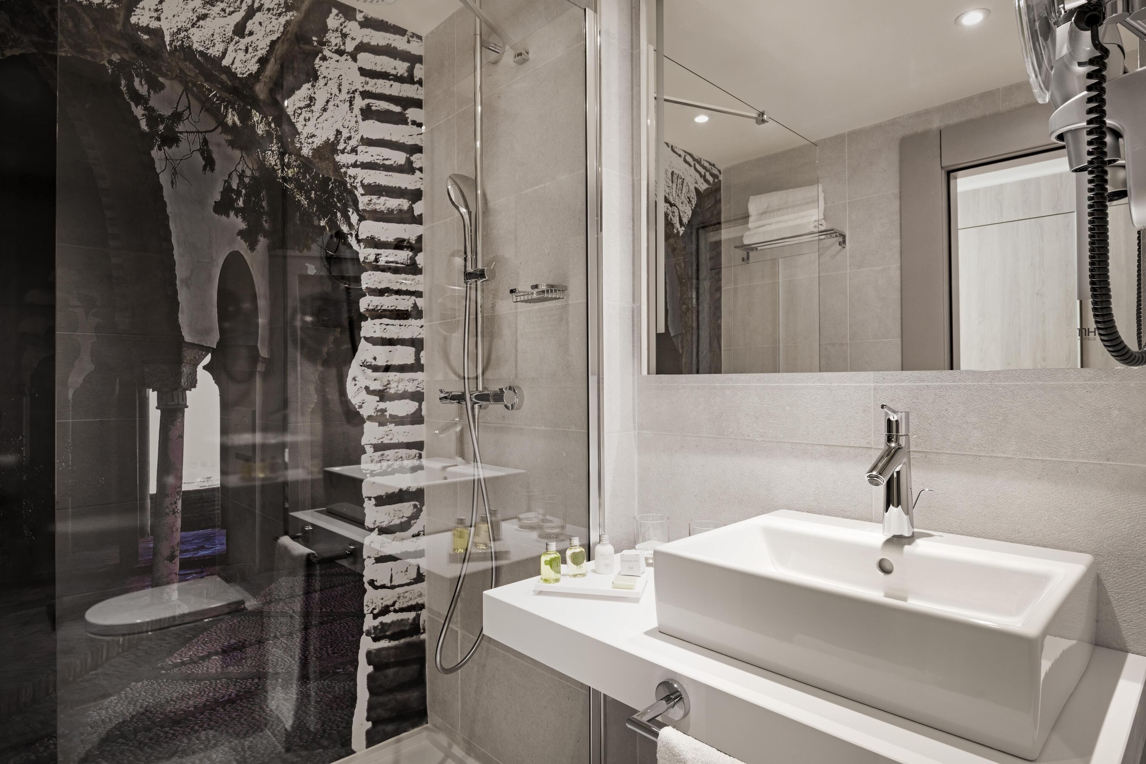 Un baño moderno con ducha envuelta en vidrio, un espejo grande y un lavamanos blanco.