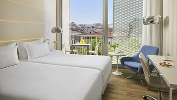 Una habitación de hotel con dos camas, un balcón con mesa y sillas, y vistas a la ciudad.