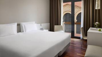 A hotel room with a large bed, a desk, and a view of an outdoor balcony with a decorative archway.