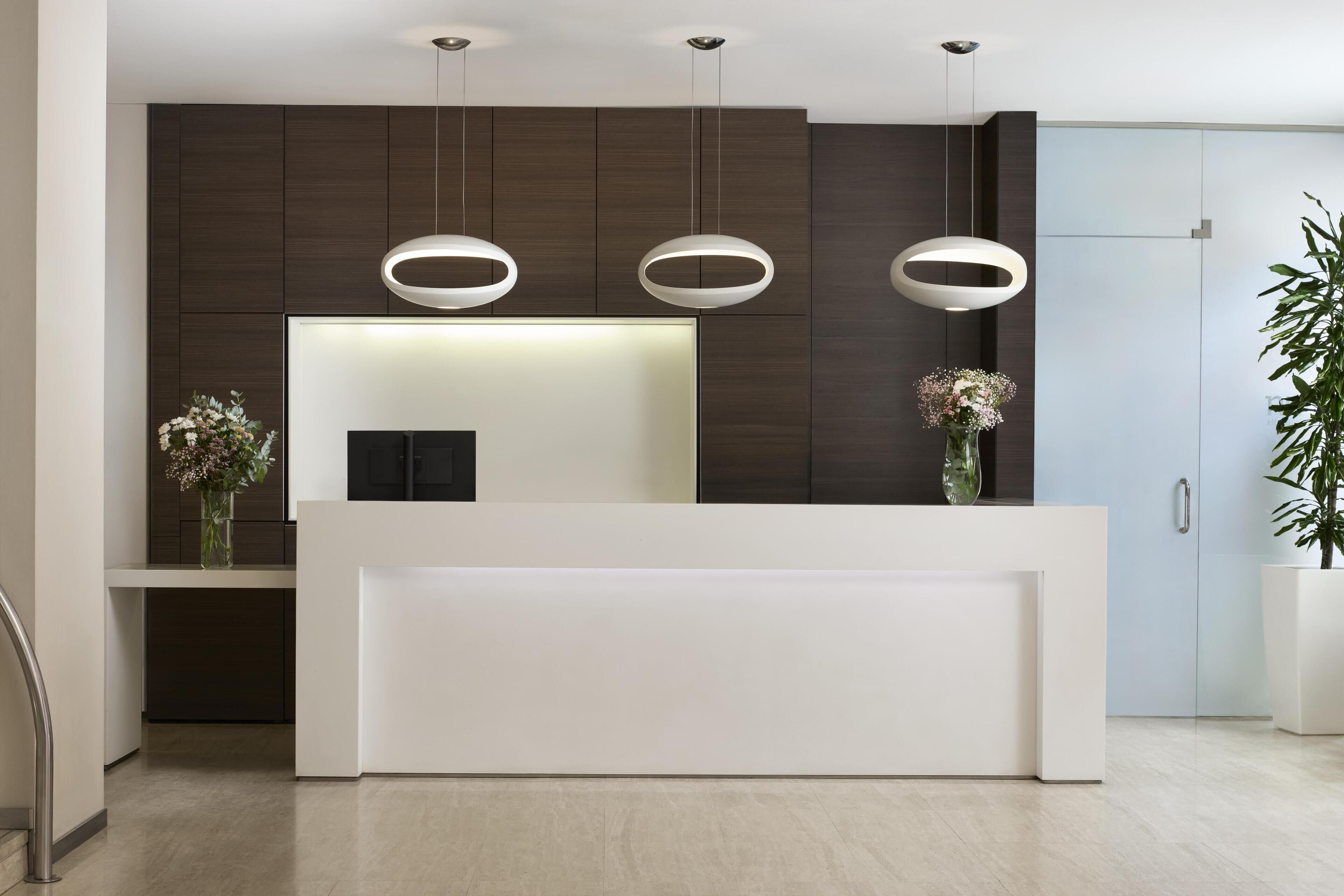 Un mostrador de recepción moderno con diseño minimalista, paneles de madera oscura y una encimera blanca.