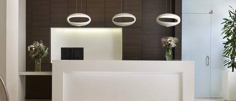 Un mostrador de recepción moderno con diseño minimalista, paneles de madera oscura y una encimera blanca.