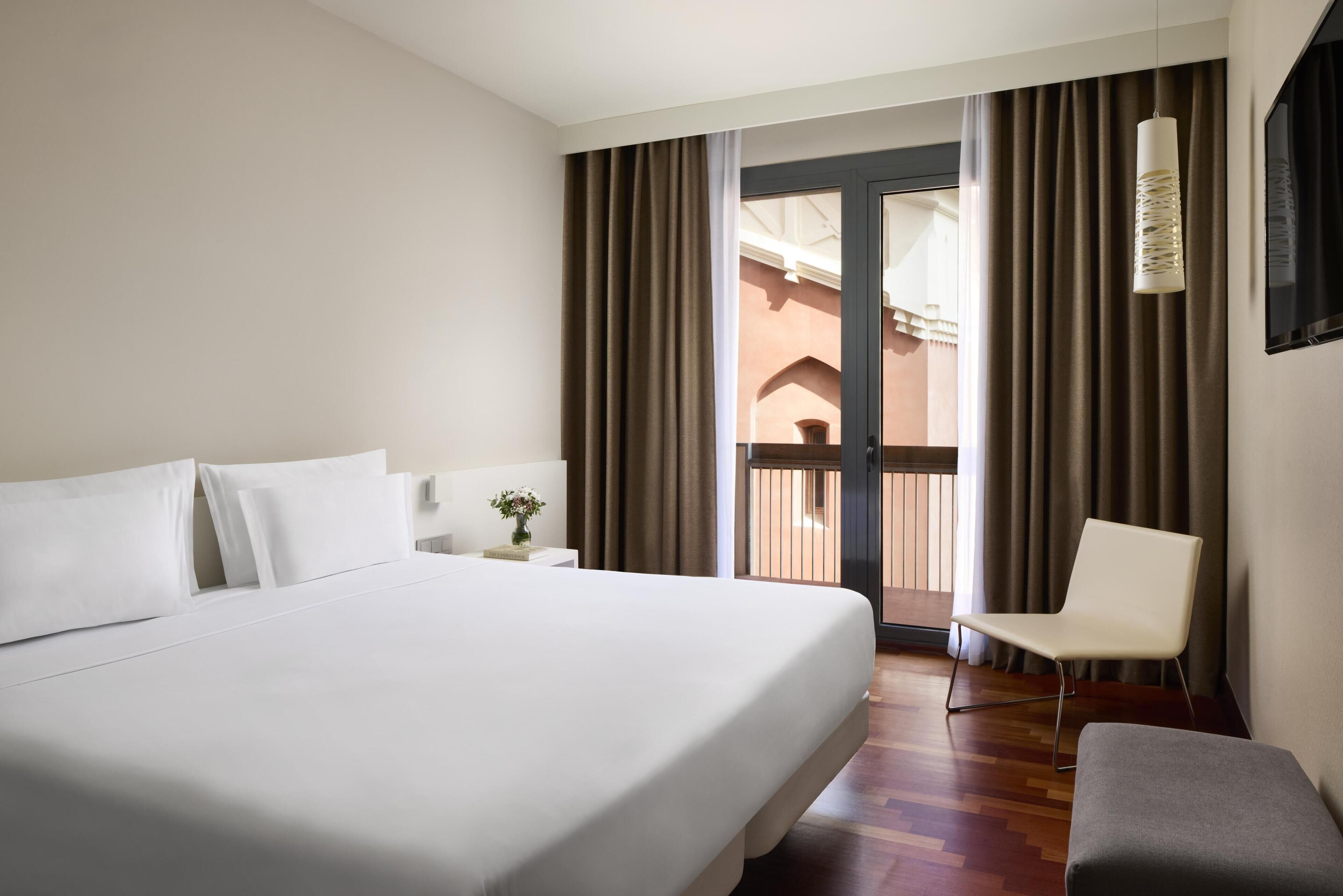 A hotel room with a large bed, a chair, a nightstand, and a view of the outside through a door.