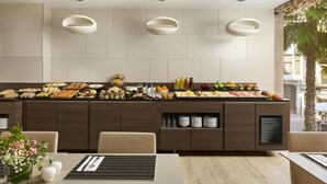 A modern kitchen with a buffet setup, including various food items and beverages, and a dining area with chairs and a table.