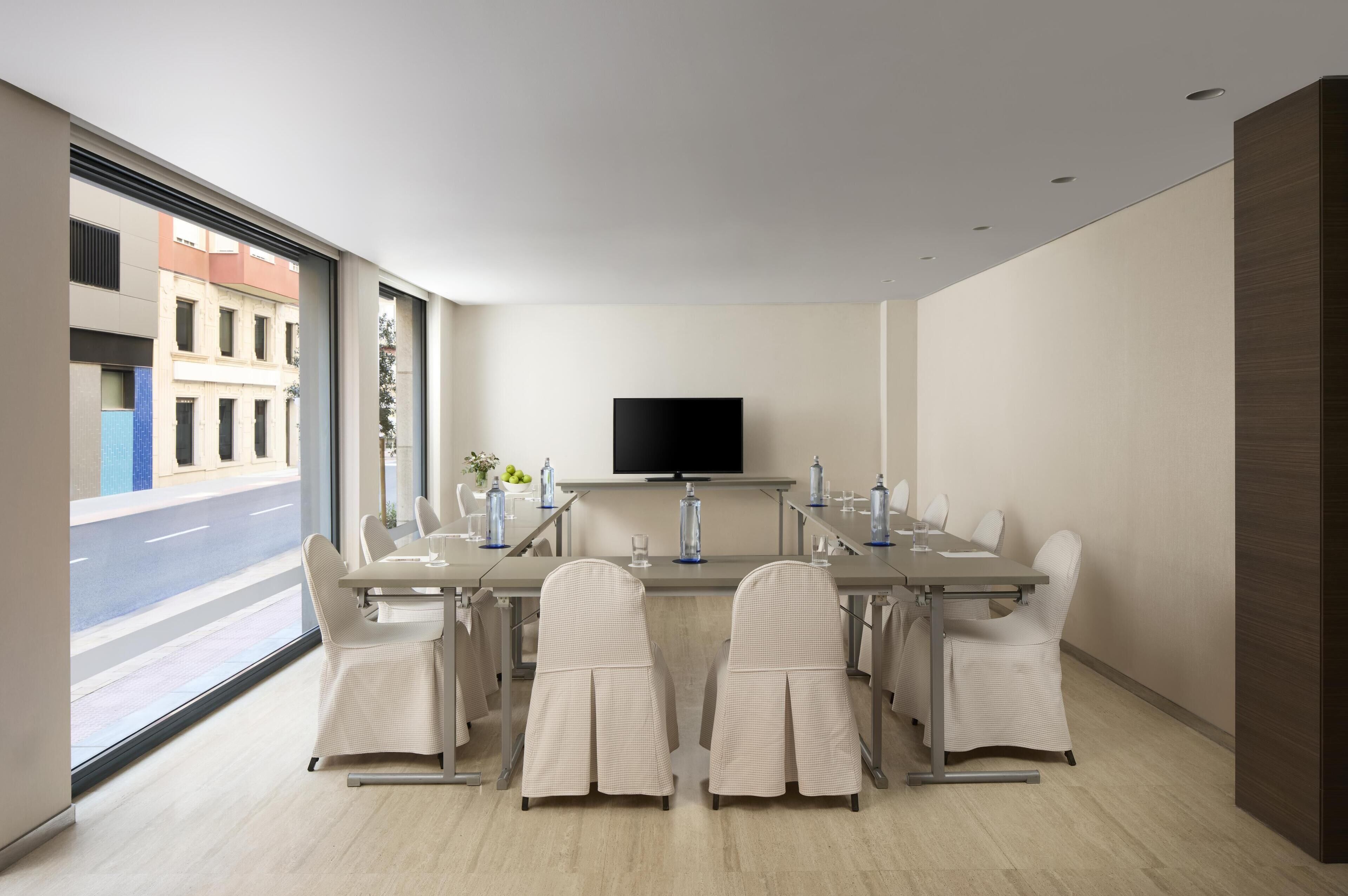 Una habitación de hotel moderna con un gran ventanal, un televisor de pantalla plana, una mesa de comedor con sillas y un minibar.