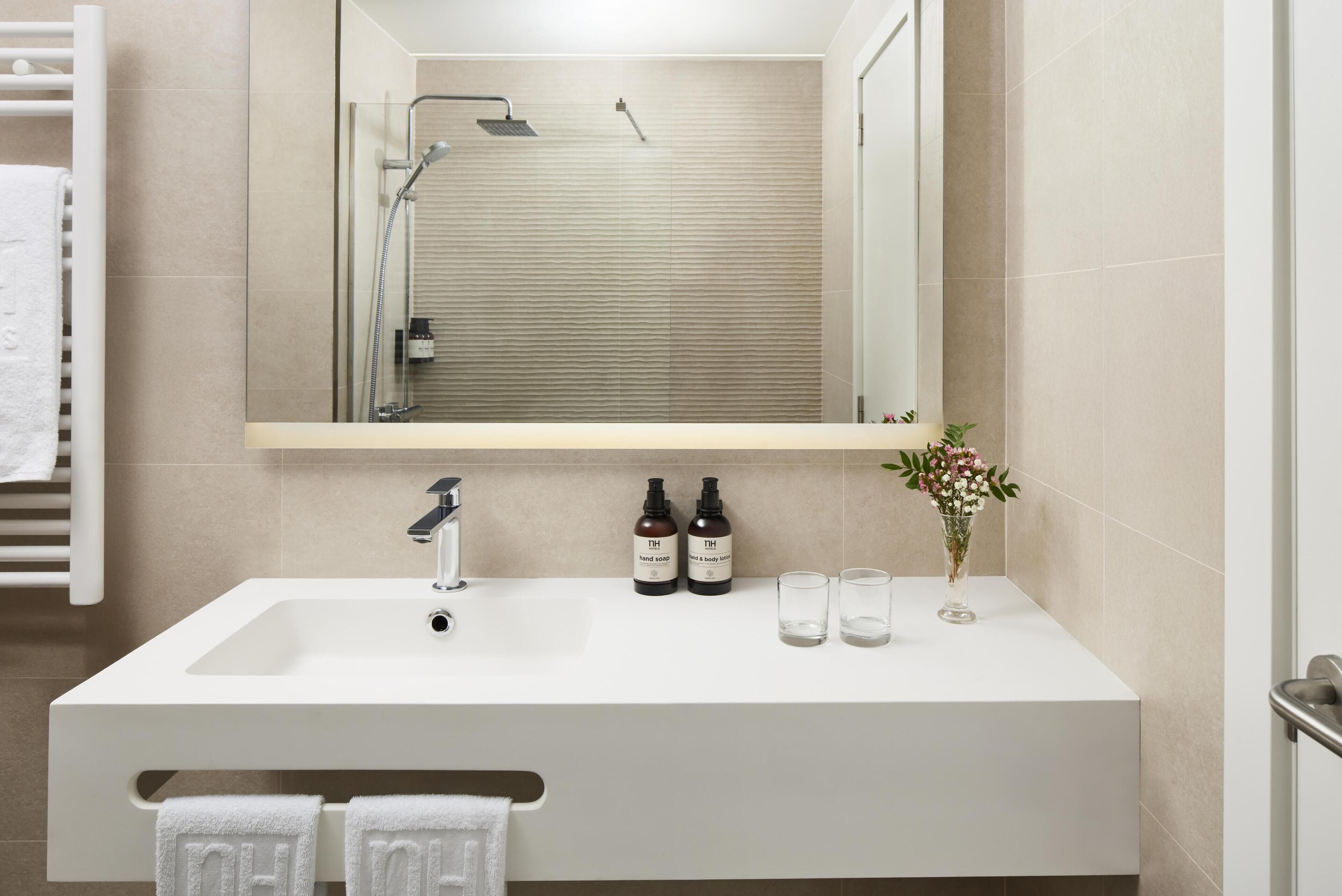 A modern bathroom with a large mirror, white sink, and two bottles of hand soap.