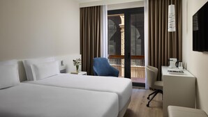 A hotel room with two beds, a desk, a chair, a TV, and a view of the outside.