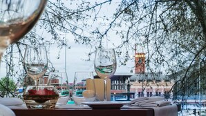 A table set with wine glasses, a bowl with a red flower, and a candle, overlooking a cityscape with buildings and a fountain. - NH Madrid Nacional (Madrid)