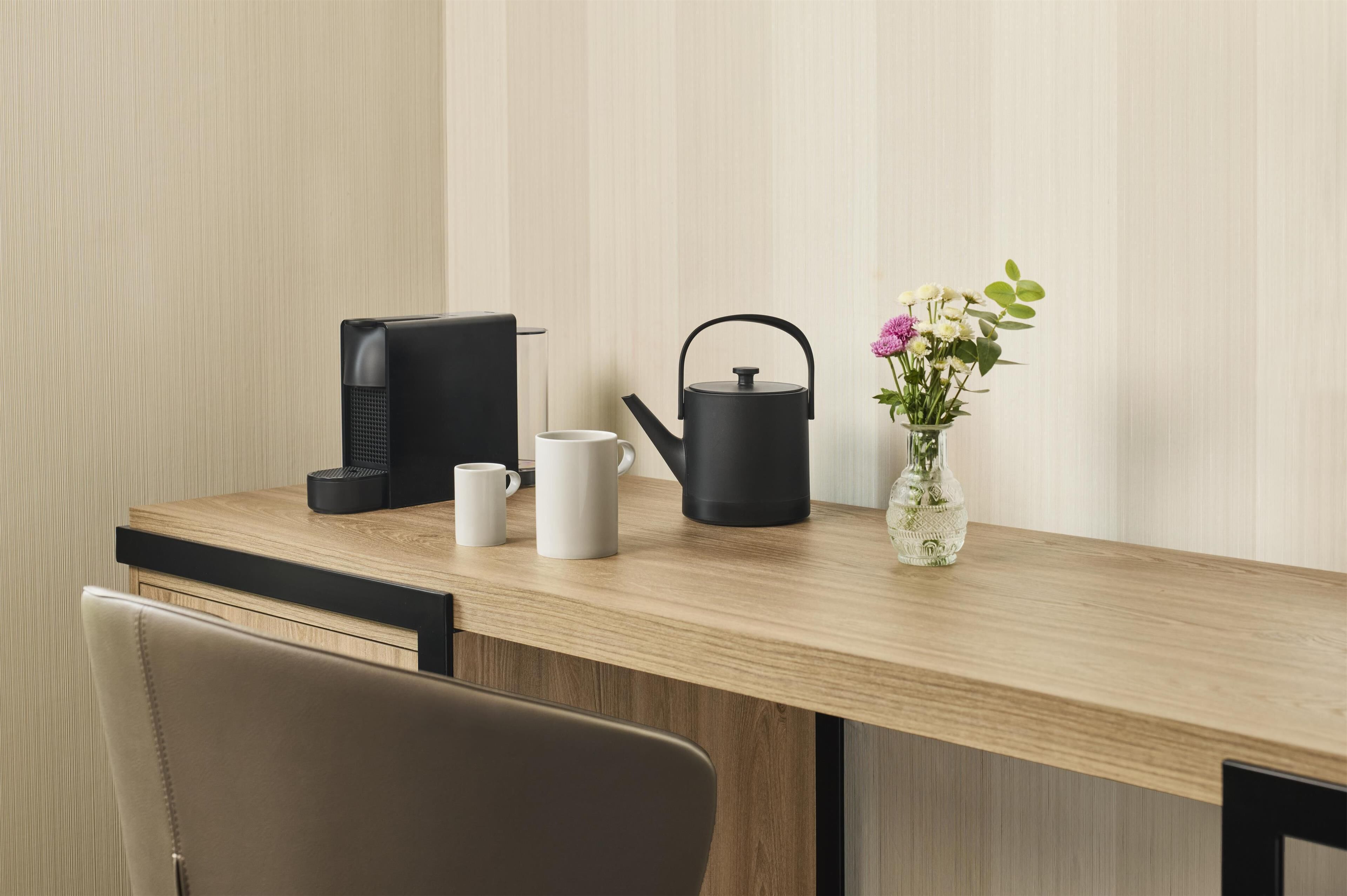 Ein Holztisch mit einem schwarzen Wasserkocher, einer weißen Tasse und einer Vase mit Blumen.