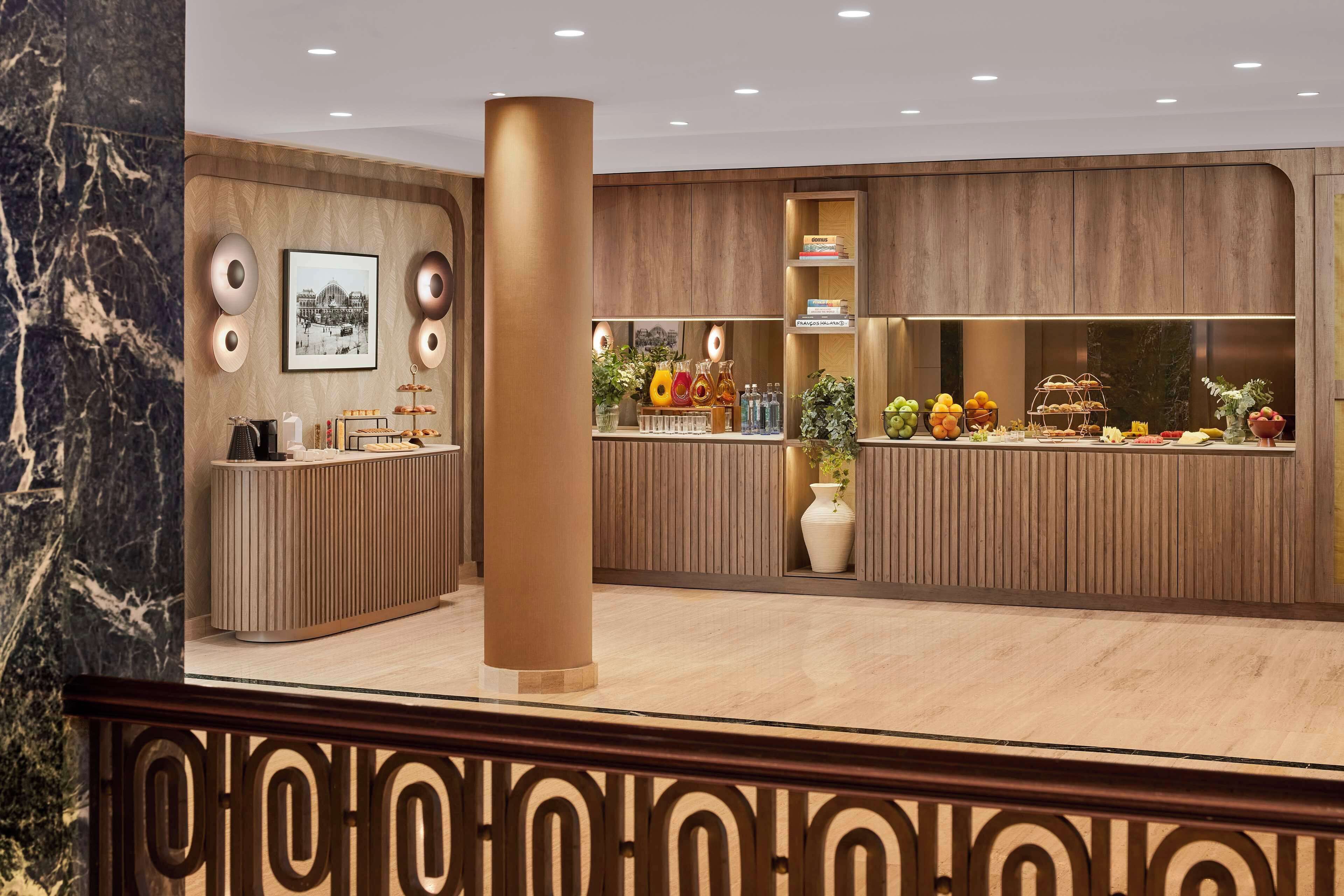 Zona de recepción con pared de mármol, mostrador de madera y una exhibición de frutas y pasteles.