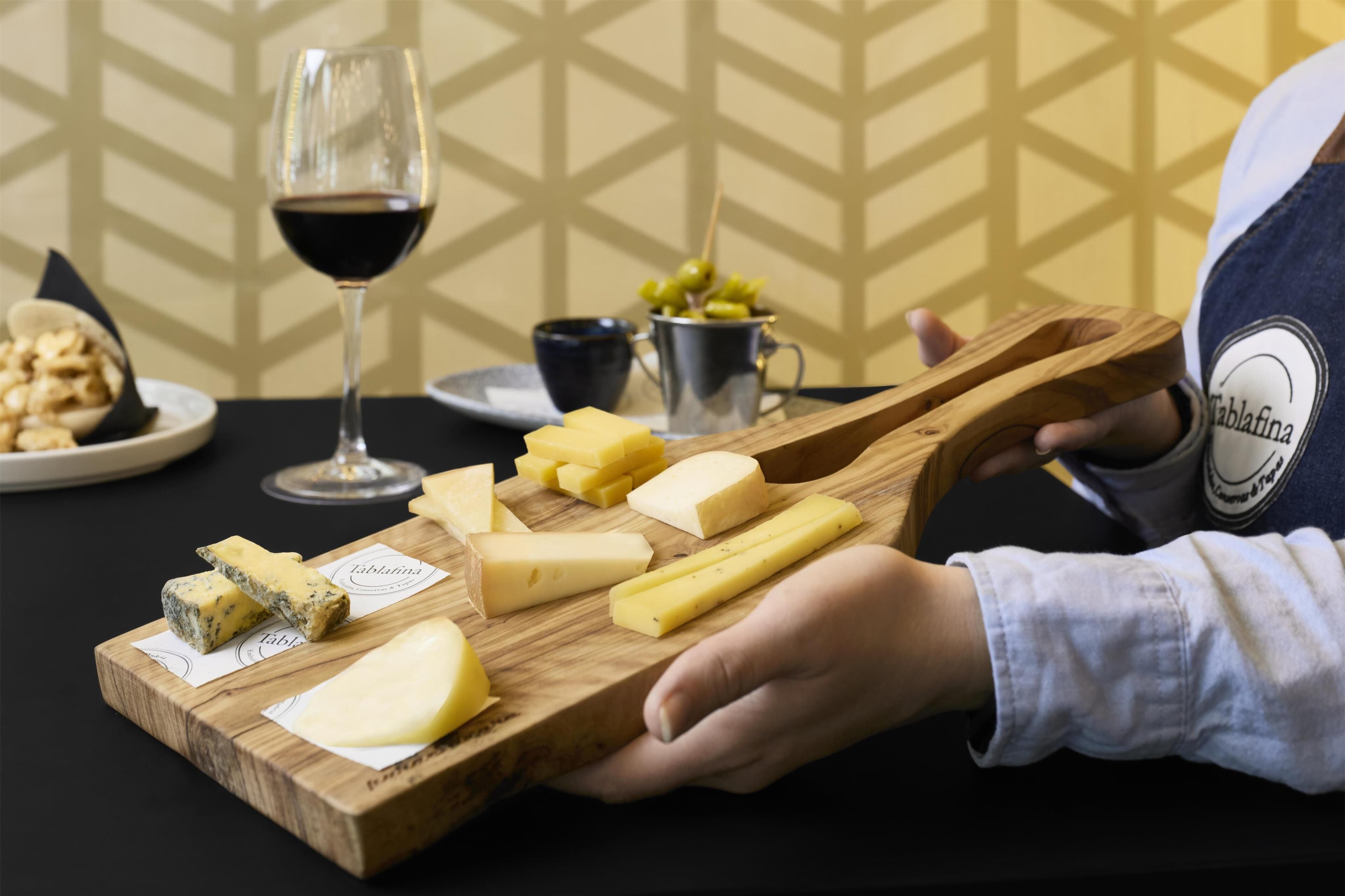 Una tabla de madera con varios quesos y una copa de vino tinto.