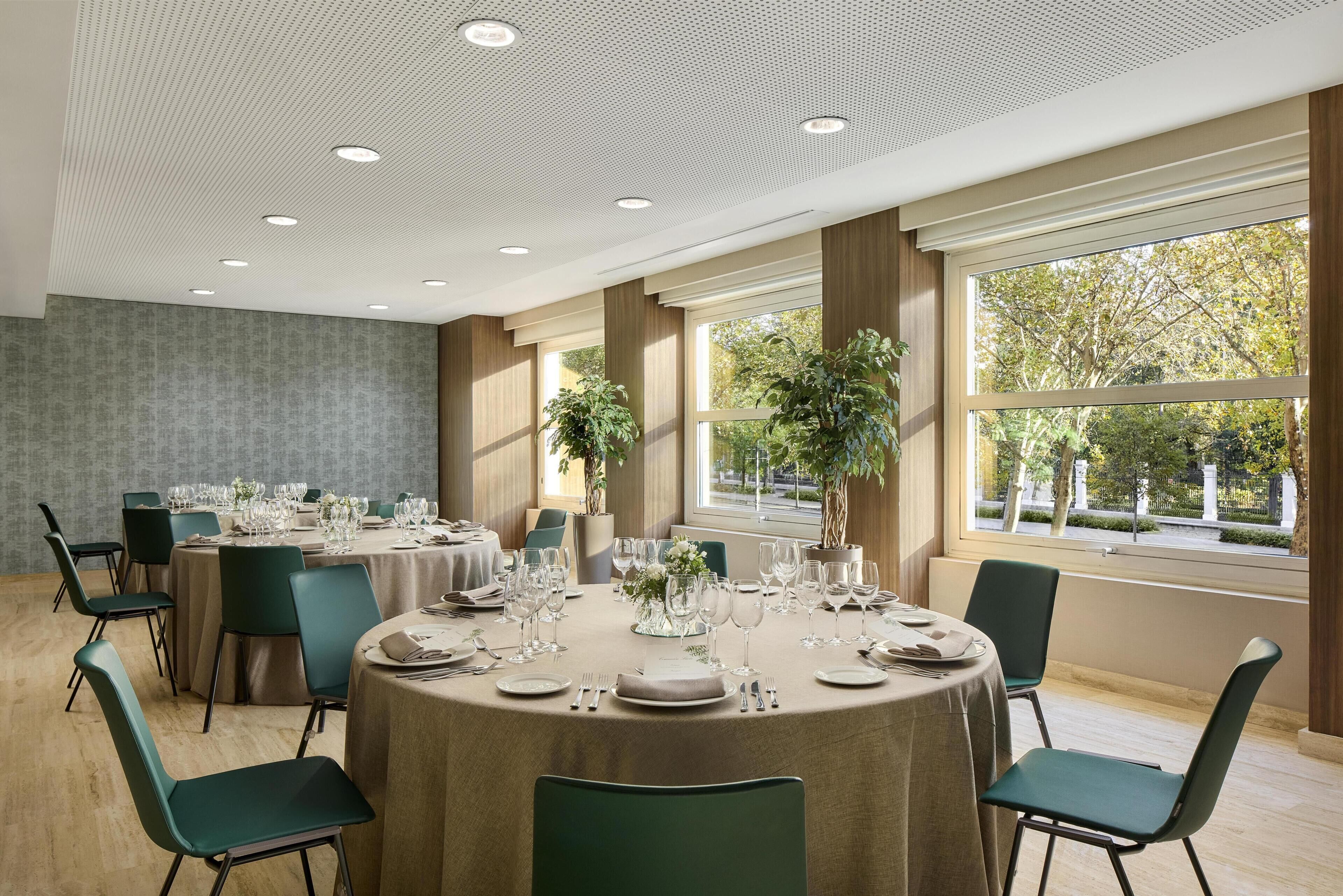 A dining area with round tables, chairs, and a large window with a view of trees.