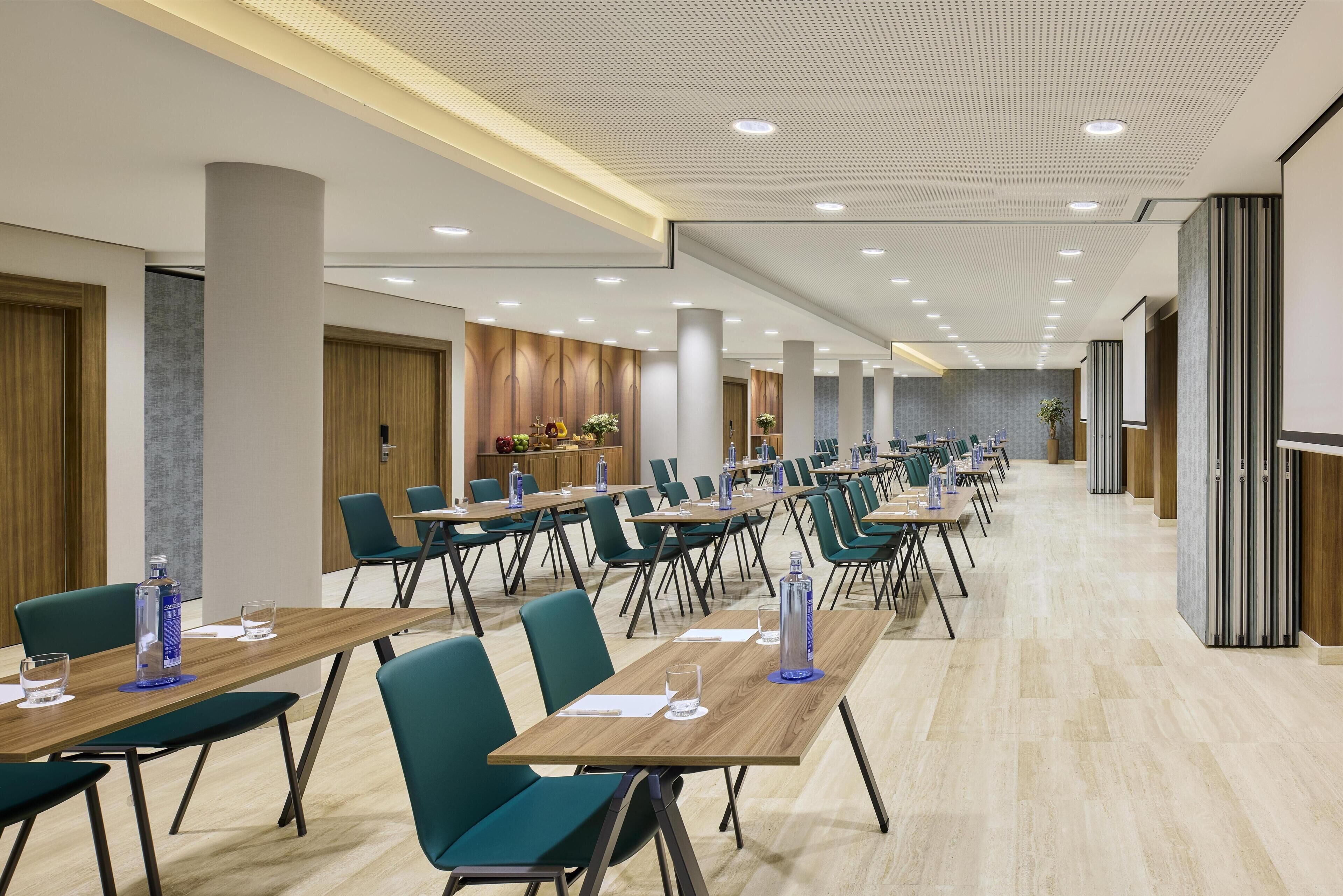 Una sala conferenze con diversi tavoli e sedie, un soffitto con illuminazione incassata e una palette di colori neutri.